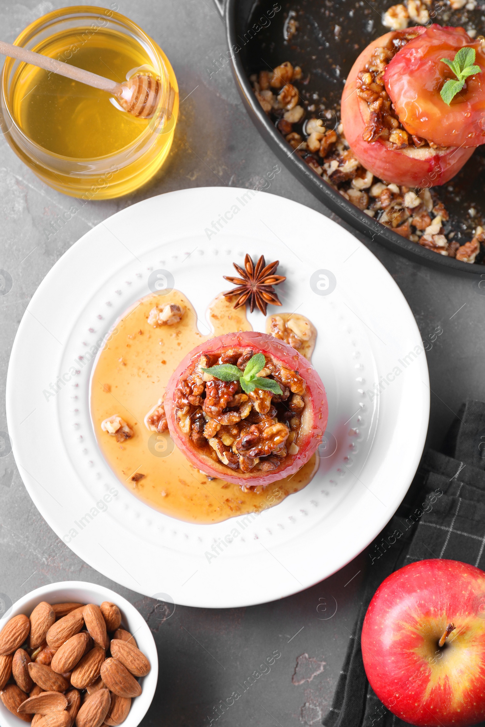 Photo of Tasty baked apples with nuts, honey and mint on gray textured table, flat lay