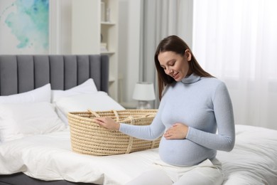 Beautiful pregnant woman with baby basket in bedroom