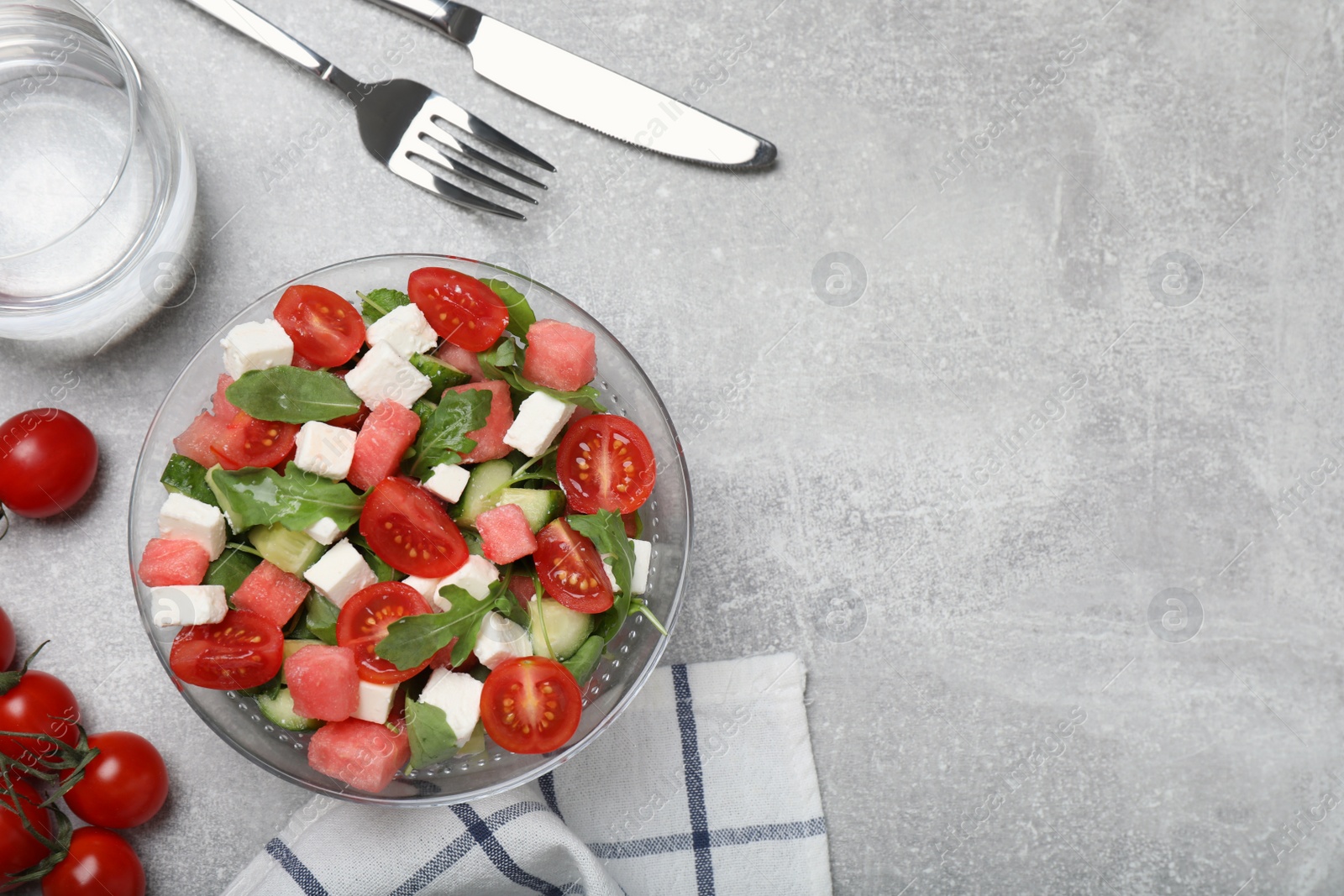 Photo of Delicious salad with watermelon, vegetables and feta cheese served on grey table, flat lay. Space for text