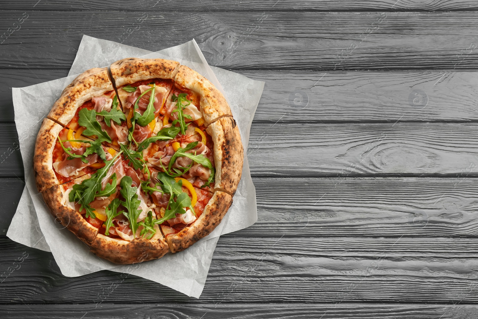 Photo of Tasty pizza with meat and arugula on grey wooden table, top view. Space for text