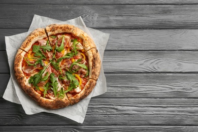 Photo of Tasty pizza with meat and arugula on grey wooden table, top view. Space for text