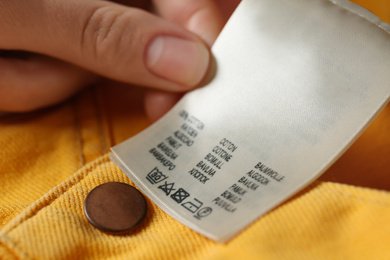 Photo of Woman reading clothing label with care symbols and material content on yellow jeans, closeup