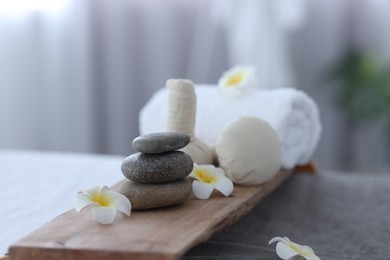 Photo of Stacked spa stones, flowers, herbal bags and towel on tray indoors, closeup