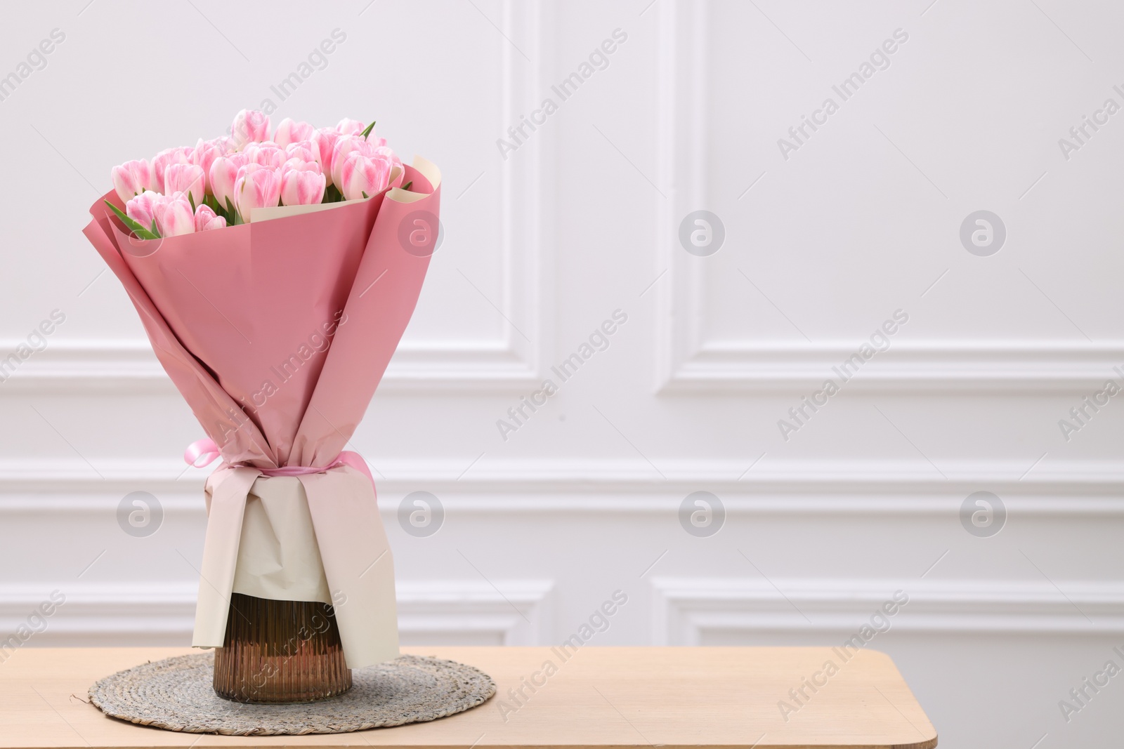 Photo of Beautiful bouquet of fresh pink tulips on wooden table near white wall. Space for text