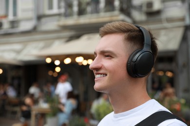 Photo of Smiling man in headphones walking outdoors. Space for text