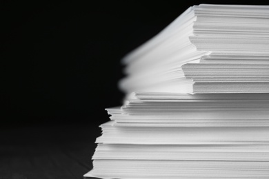 Photo of Stack of blank paper on table against black background, closeup