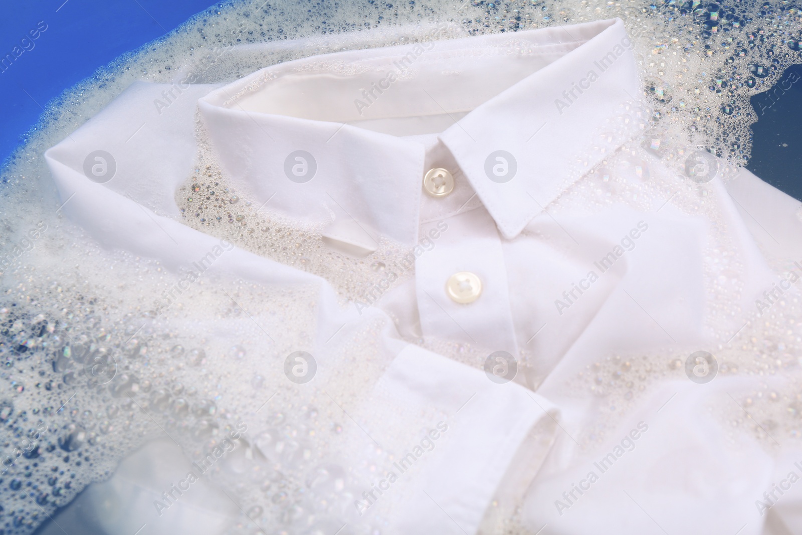 Photo of White shirt in suds, closeup. Hand washing laundry