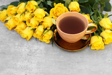 Photo of Cup of tea and beautiful yellow roses on light table, space for text