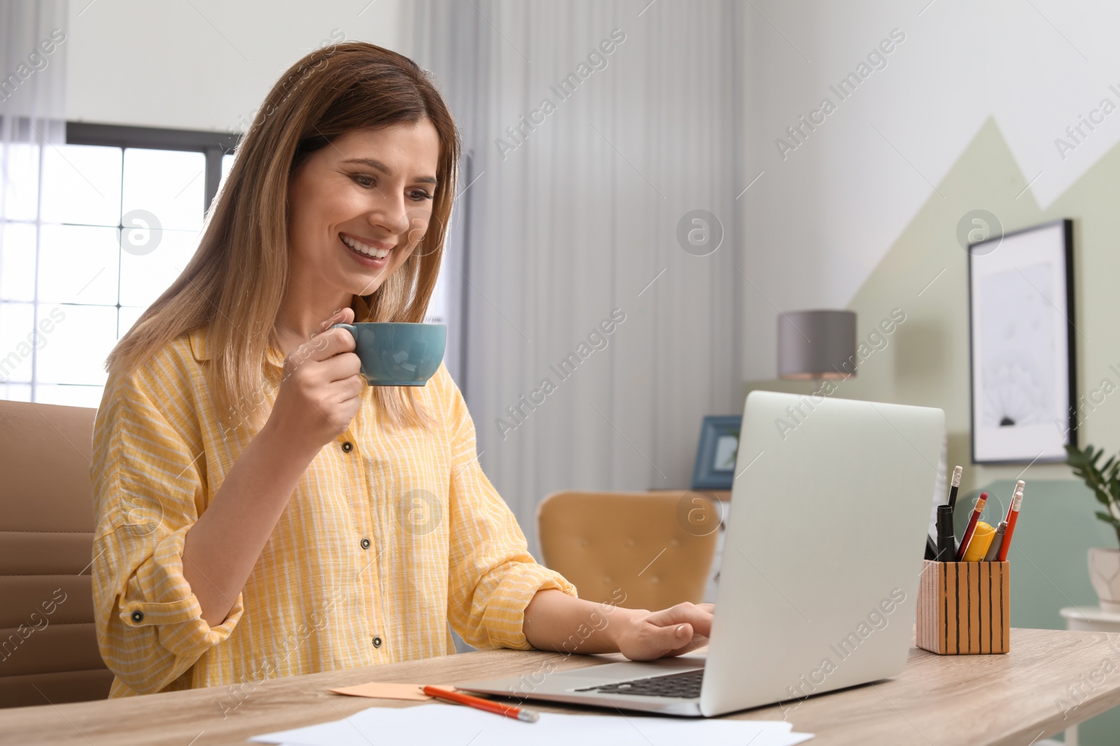 Photo of Young woman working with laptop at desk in home office