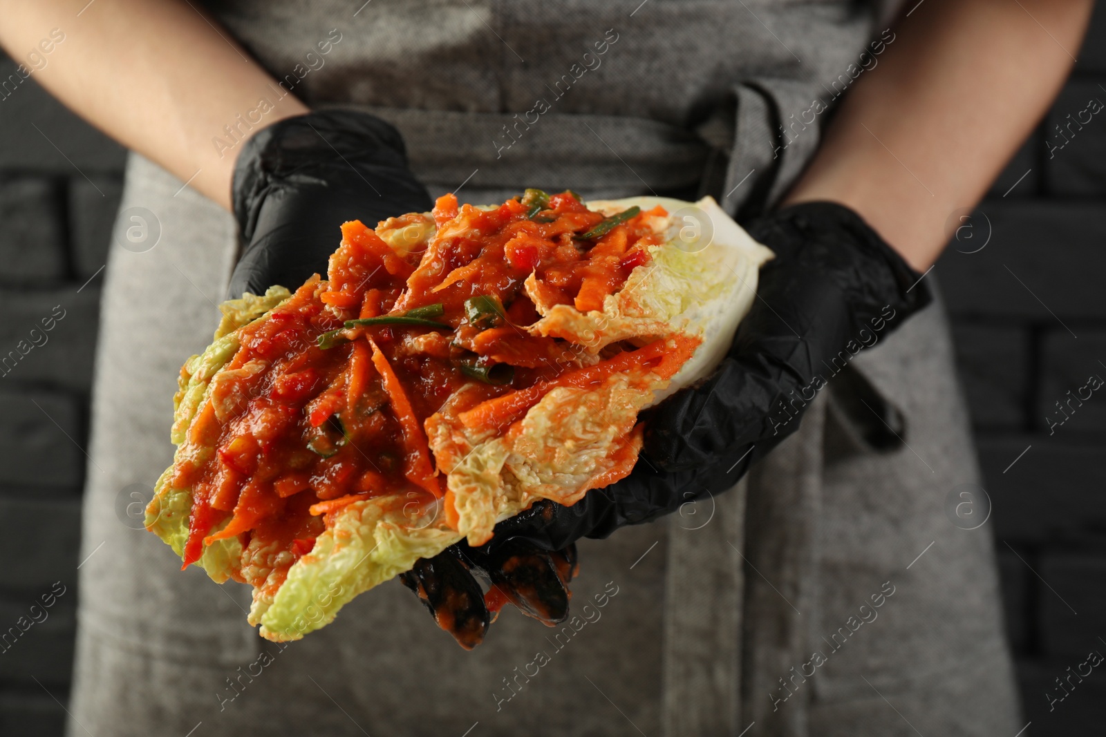 Photo of Woman preparing spicy cabbage kimchi indoors, closeup