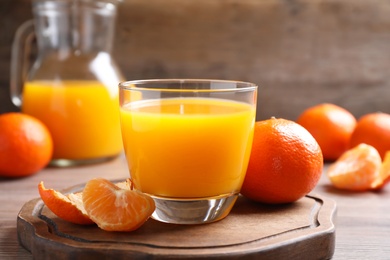 Glass of fresh tangerine juice and fruits on wooden board