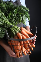 Photo of Woman holding basket with ripe carrots on black background, closeup