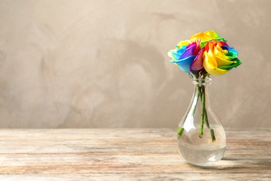 Photo of Vase with amazing rainbow rose flowers on table