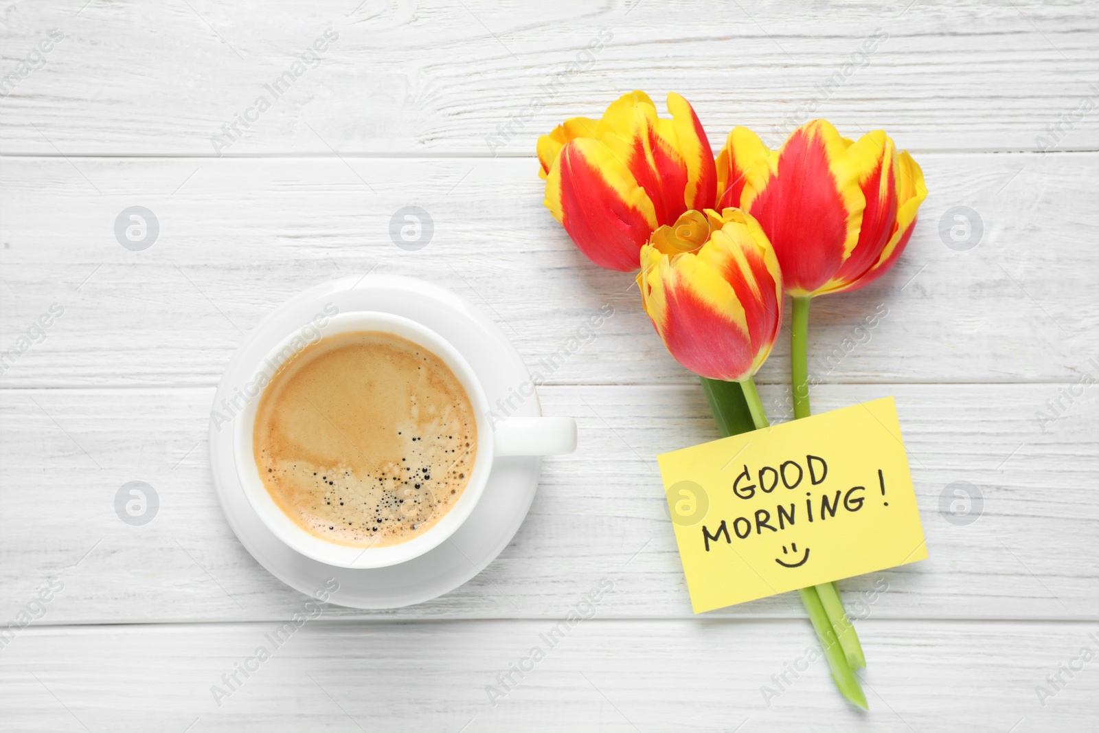 Photo of Delicious coffee, flowers and card with GOOD MORNING wish on white wooden table, flat lay