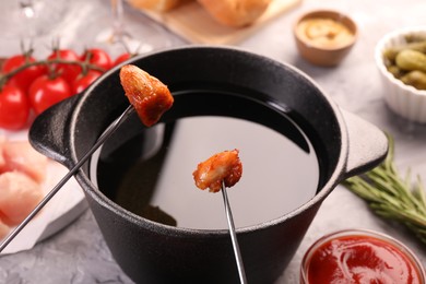 Photo of Fondue pot, forks with fried meat pieces and other products on grey textured table, closeup