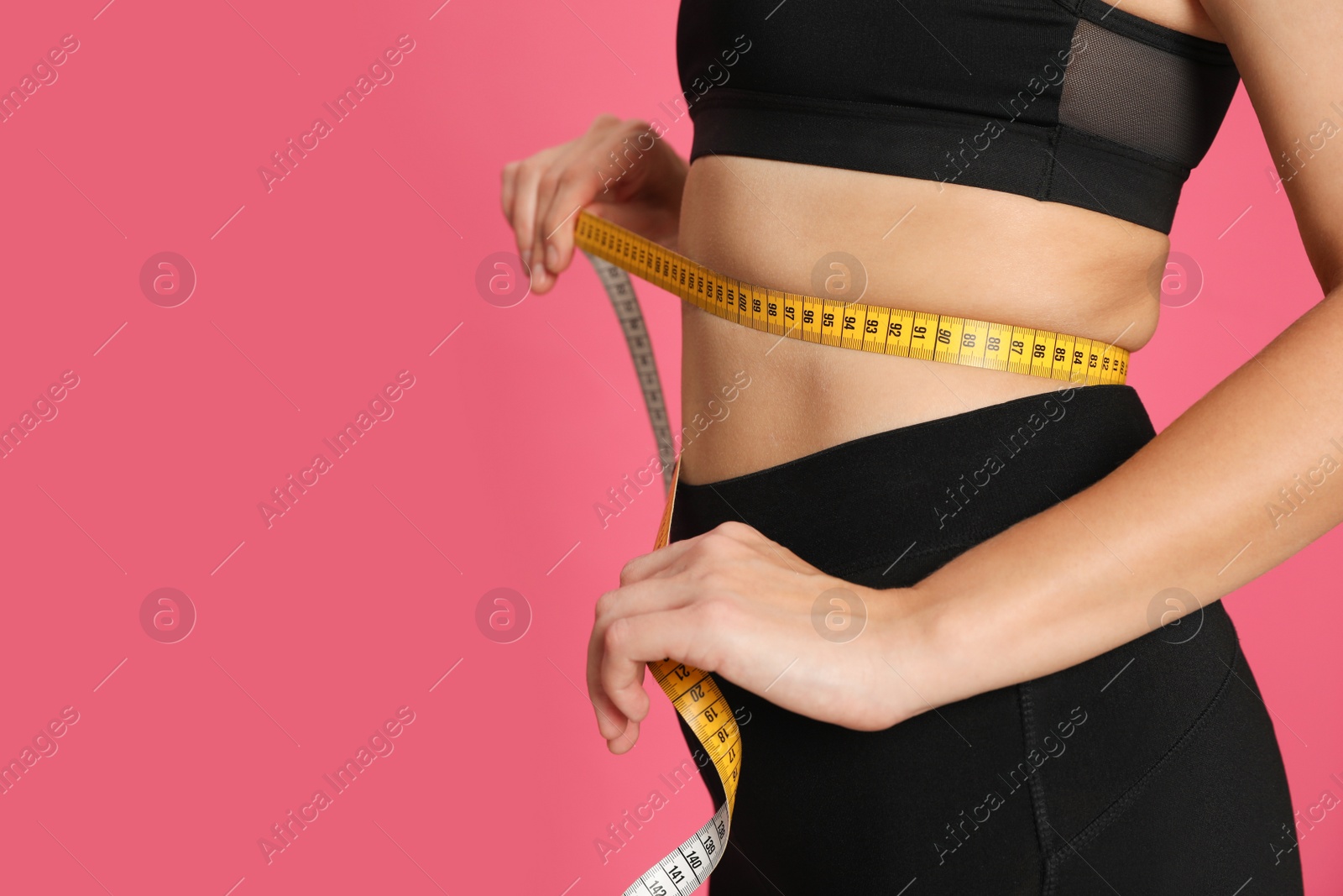 Photo of Woman measuring waist with tape on pink background, closeup. Space for text