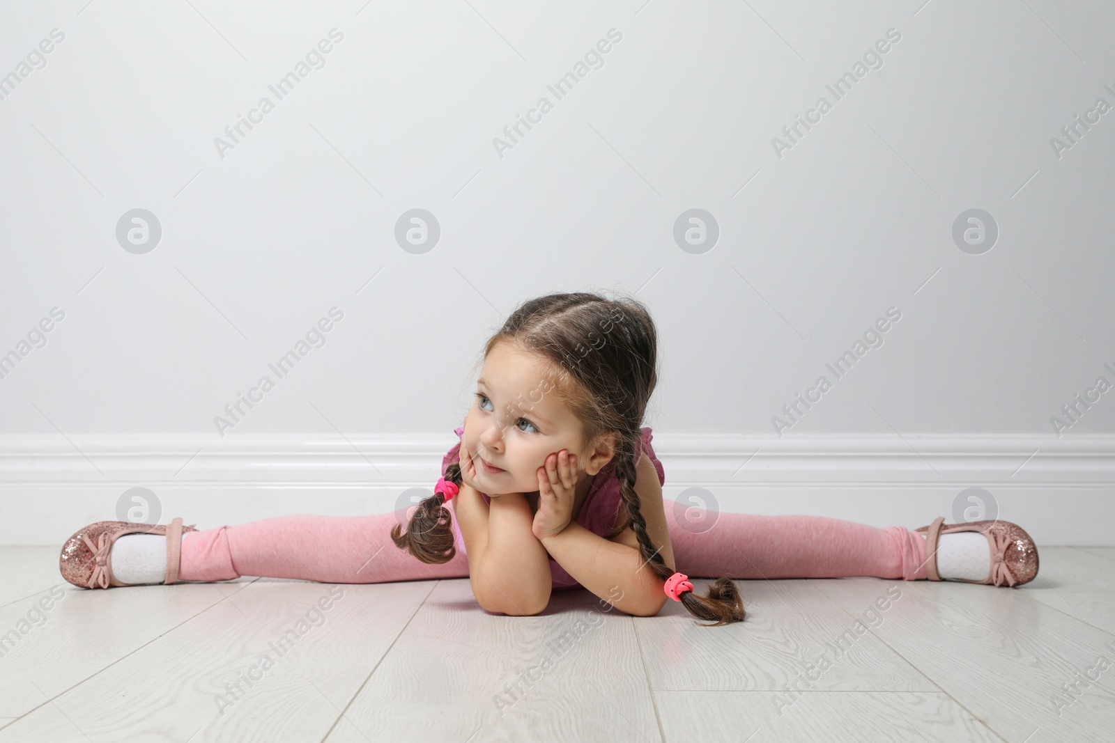 Photo of Cute little girl on floor near light grey wall