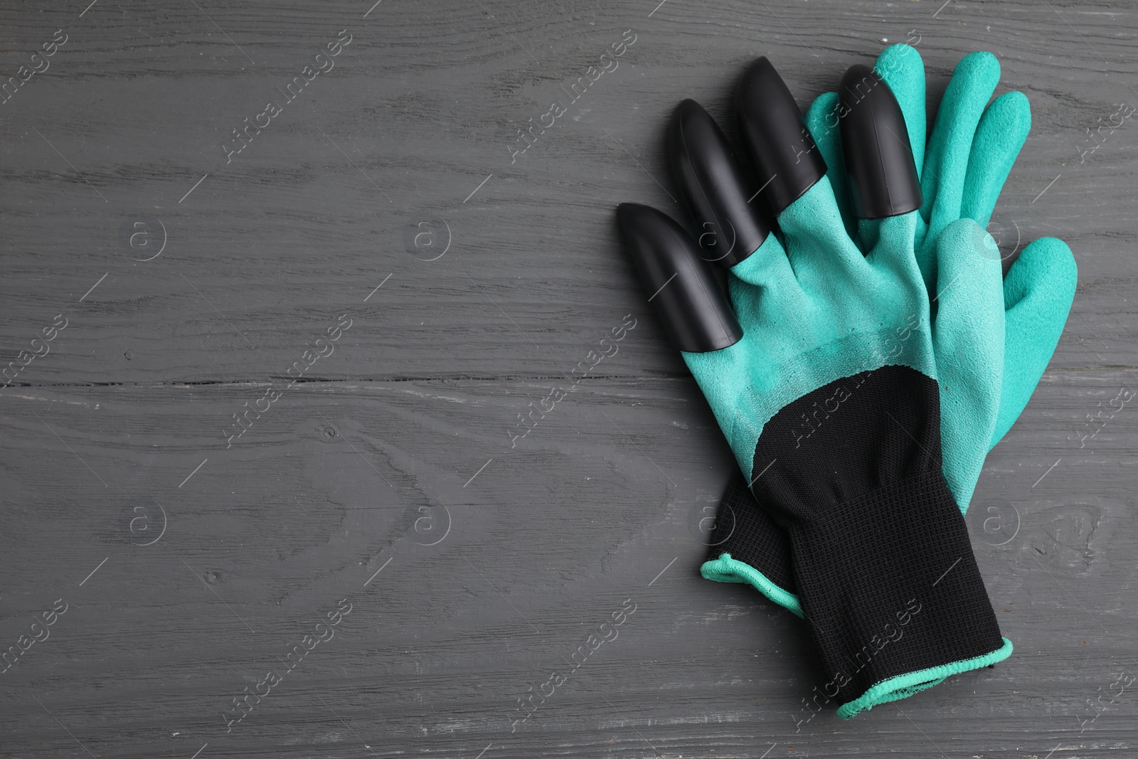 Photo of Pair of claw gardening gloves on grey wooden table, top view. Space for text