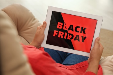 Photo of Woman using tablet with Black Friday announcement while sitting in armchair, closeup