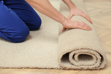 Photo of Worker rolling out new carpet flooring indoors, closeup