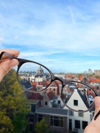 Image of Vision correction. Woman looking through glasses and seeing cityscape clearer