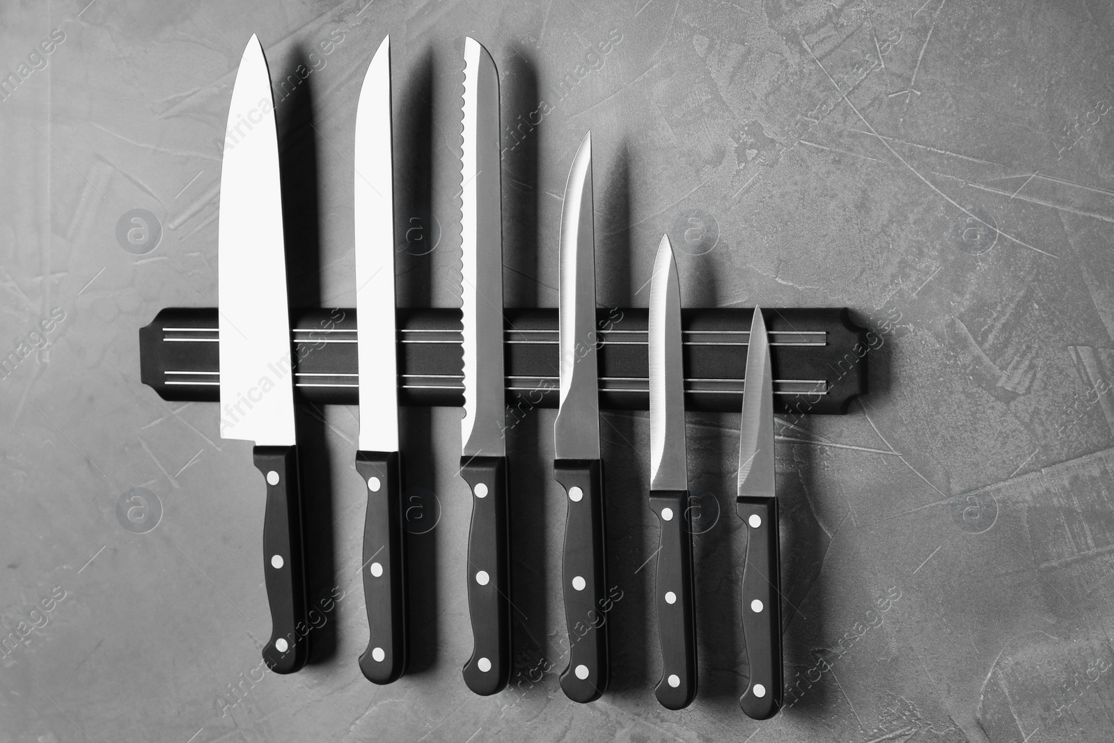 Photo of Magnetic holder with set of knives on grey stone background