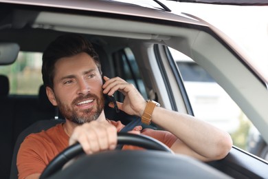 Photo of Happy bearded man talking on smartphone in car, view through windshield