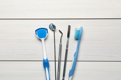 Photo of Tongue cleaner, dental instruments and toothbrush on white wooden table, flat lay