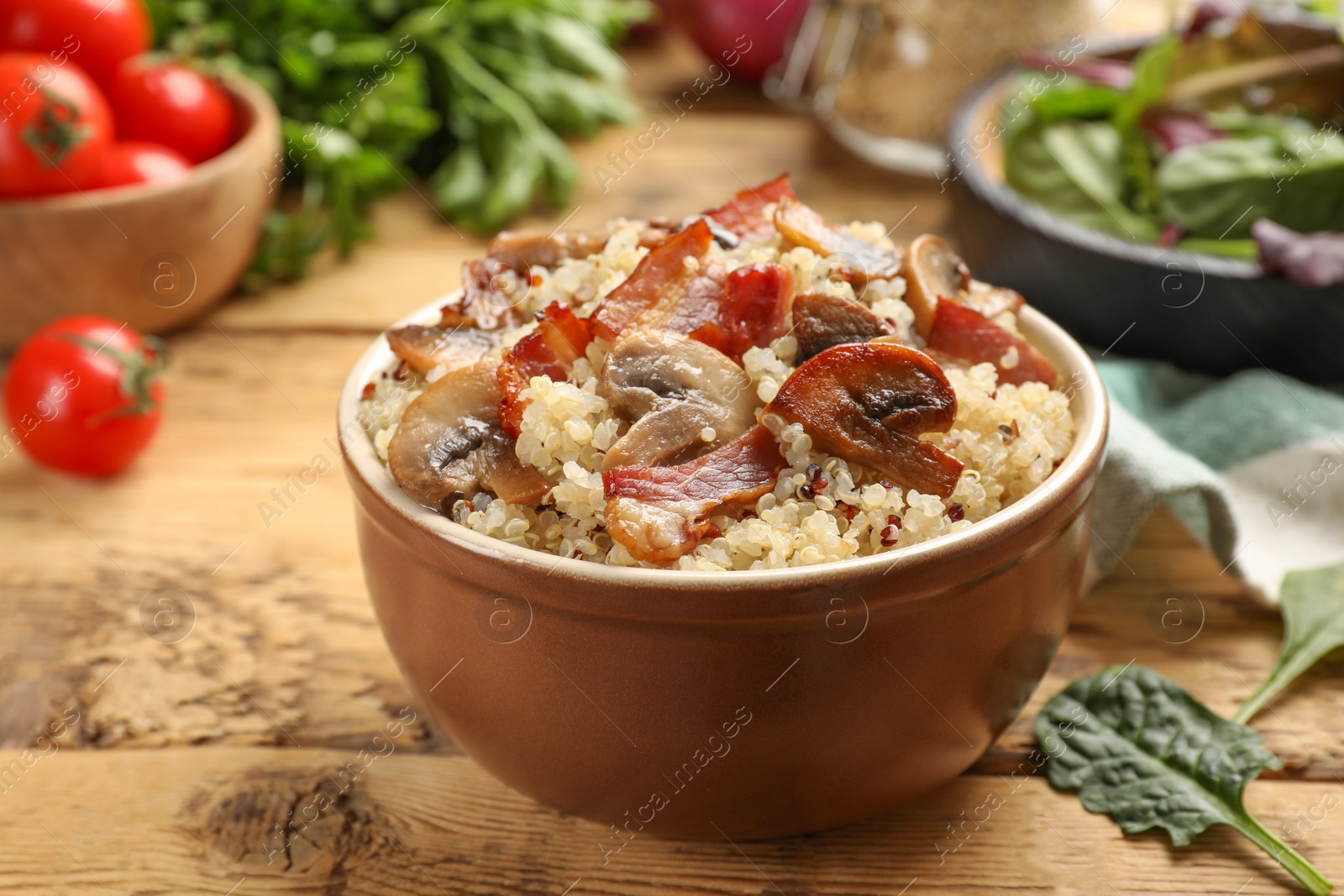 Photo of Tasty quinoa porridge with fried bacon and mushrooms in bowl on wooden table, closeup