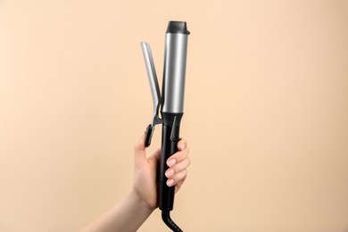 Hair styling appliance. Woman holding curling iron on beige background, closeup