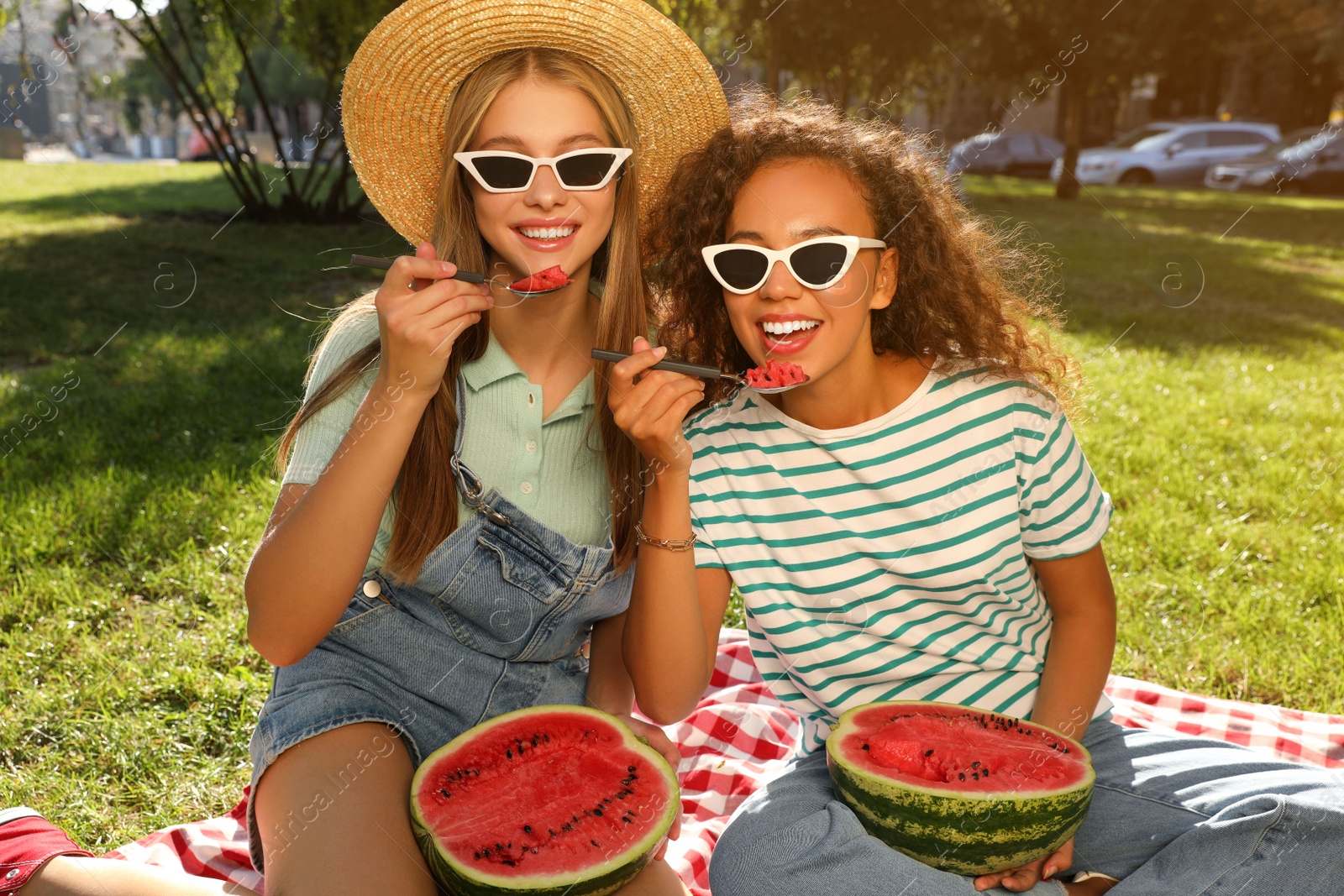 Photo of Happy girls eating watermelon on picnic blanket in park