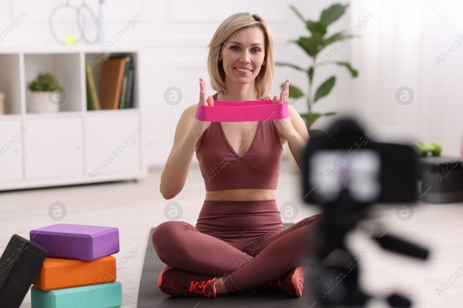 Photo of Smiling sports blogger with with resistance bands recording fitness lesson with camera at home