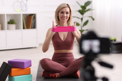 Smiling sports blogger with with resistance bands recording fitness lesson with camera at home