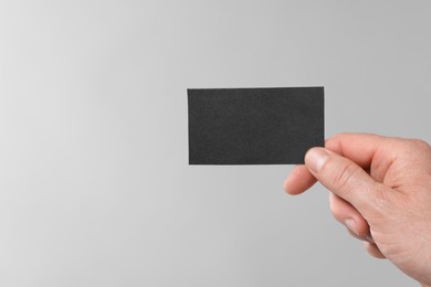 Man holding blank business card on light grey background, closeup. Space for text