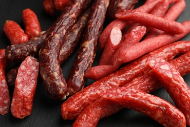 Photo of Different thin dry smoked sausages on black table, closeup