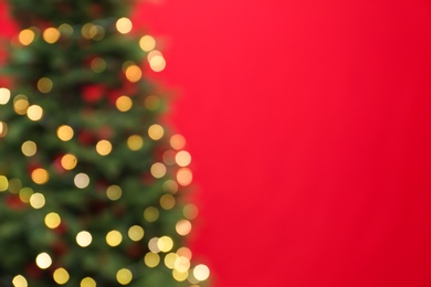 Blurred view of beautiful Christmas tree with fairy lights on red background