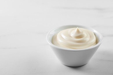 Photo of Tasty mayonnaise sauce in bowl on white table, closeup. Space for text