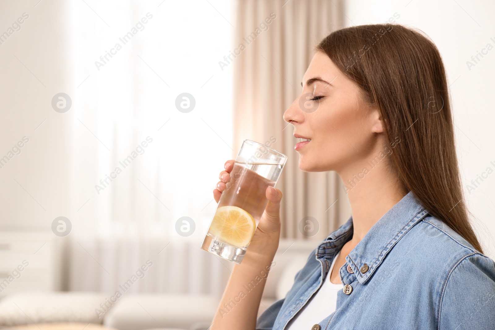 Photo of Young woman drinking lemon water at home. Space for text