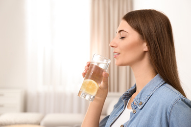 Young woman drinking lemon water at home. Space for text
