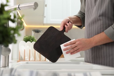 Photo of Man wiping dark wooden cutting board with paper napkin at sink in kitchen, closeup