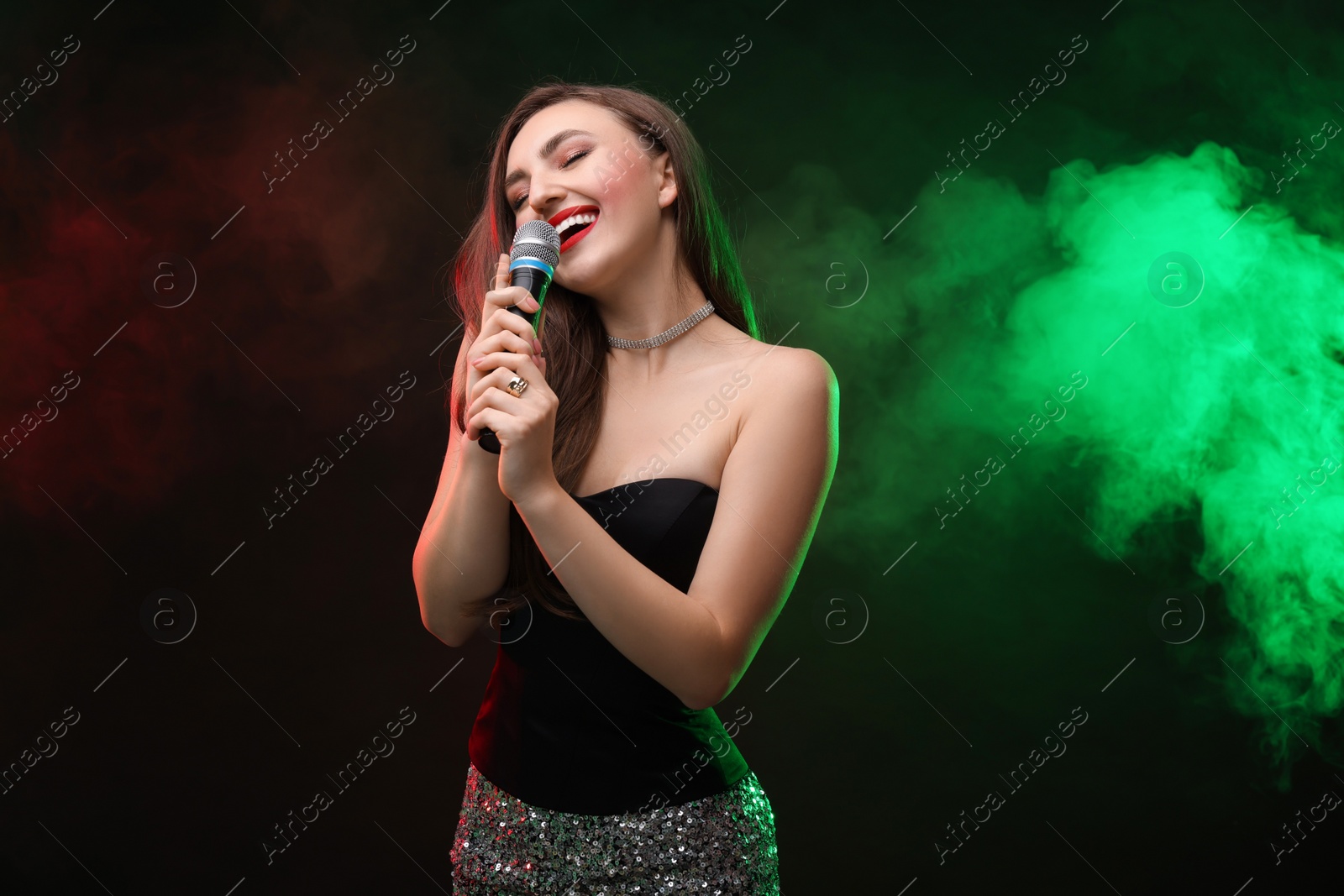 Photo of Beautiful woman with microphone singing in color lights on dark background