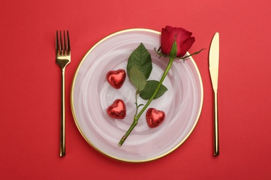 Photo of Beautiful table setting with rose for Valentine's Day dinner on red background, flat lay