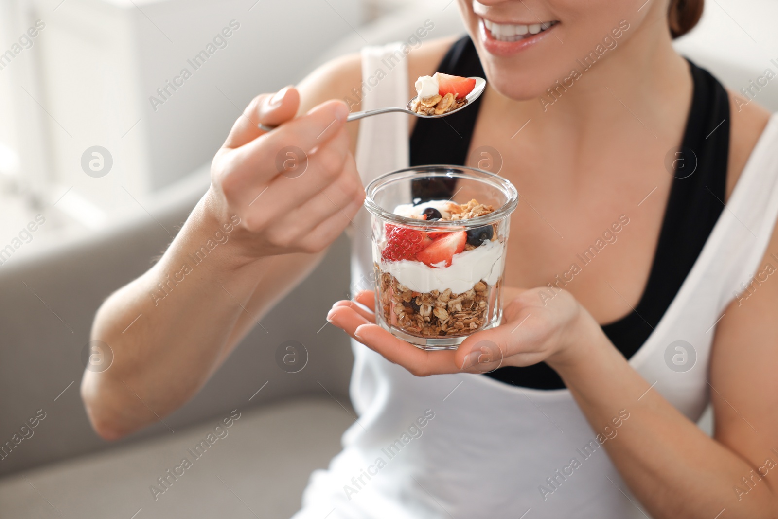 Photo of Woman eating tasty granola with fresh berries and yogurt at home, closeup