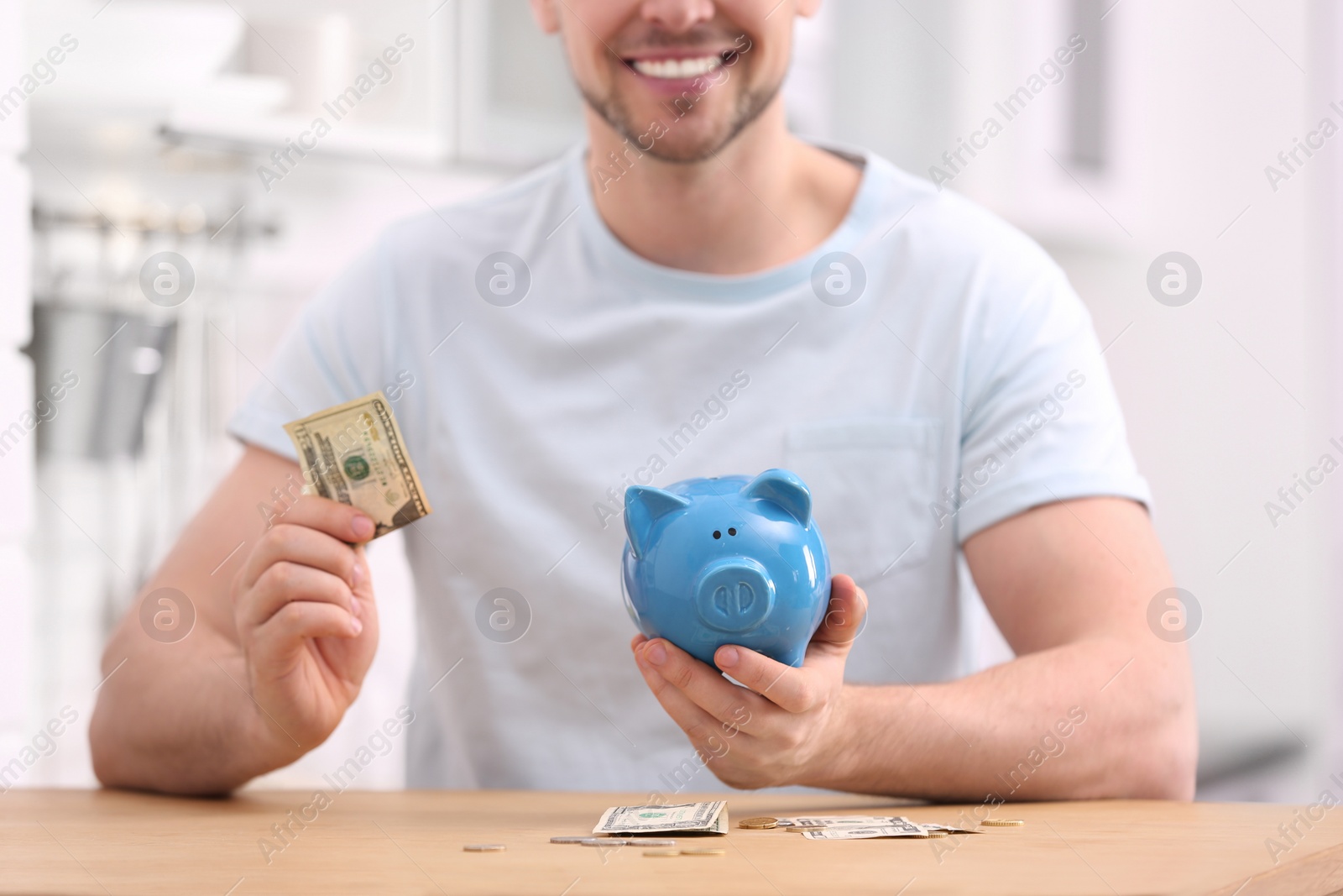 Photo of Man with piggy bank and money at home, closeup