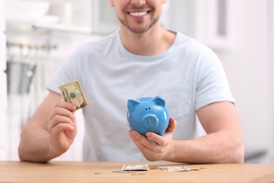 Man with piggy bank and money at home, closeup