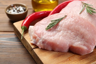 Photo of Pieces of raw pork meat, rosemary and chili peppers on wooden table, closeup