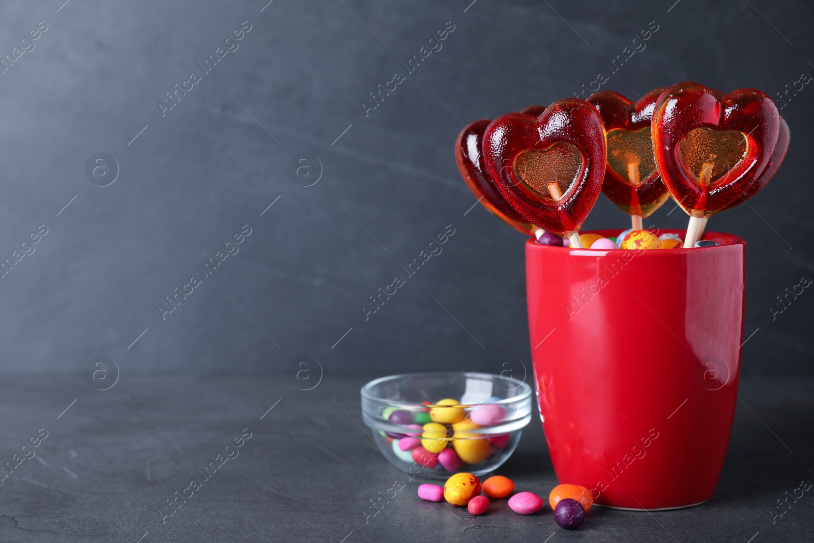 Photo of Delicious heart shaped lollipops and dragees on black table. Space for text