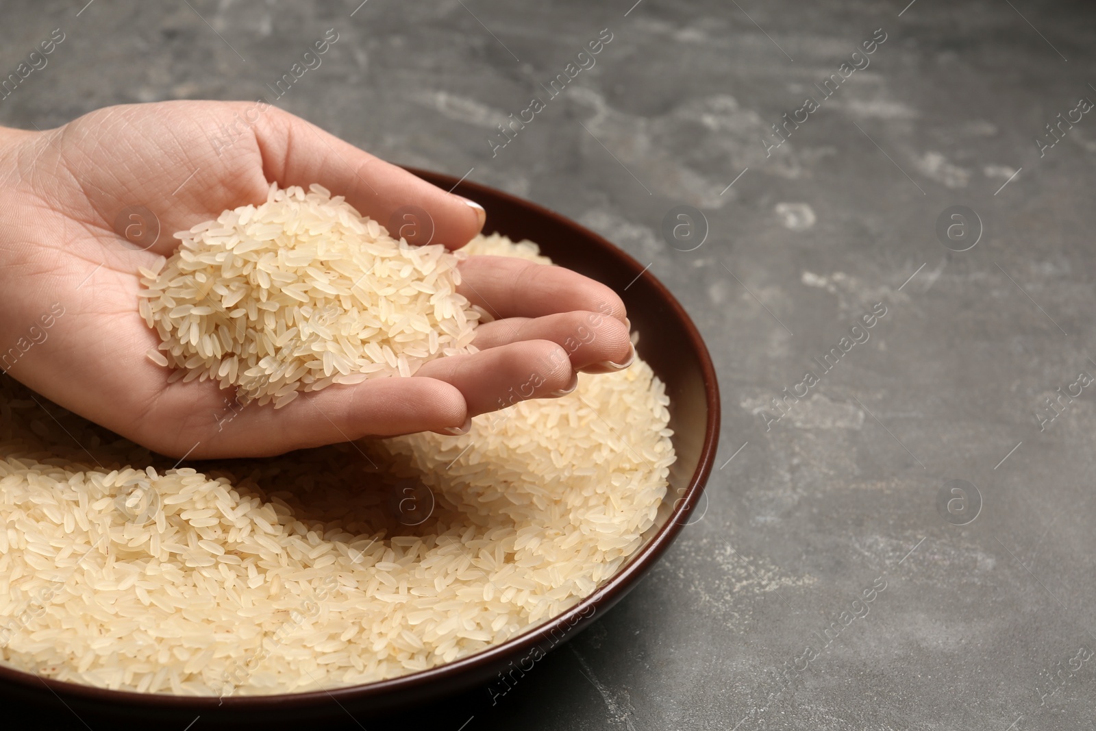 Photo of Woman holding grains near plate with parboiled rice on table, space for text