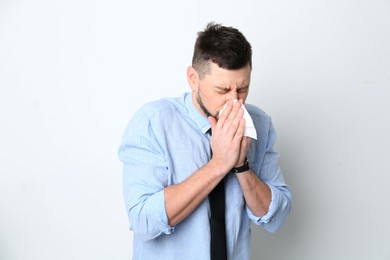 Photo of Man with tissue suffering from runny nose on white background