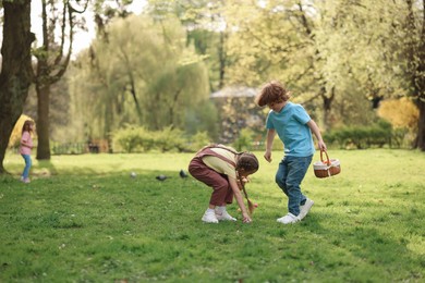 Photo of Easter celebration. Cute little children hunting eggs outdoors, space for text